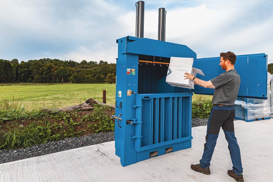 operator loading a cardboard box into the 450 baler chamber.